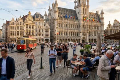 Piazza storica europea affollata al tramonto con persone che usano lo smartphone e bandiere di diversi Paesi UE: il rapporto BEREC sul consolidamento delle telco europee