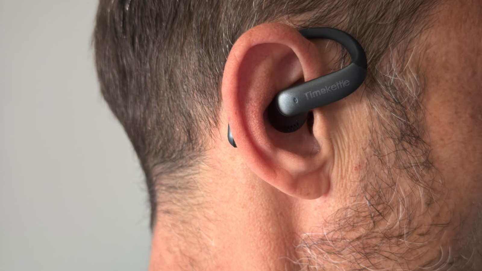Auricolare Timekettle LiveTalk indossato all'orecchio, con l'archetto aperto e il logo in vista